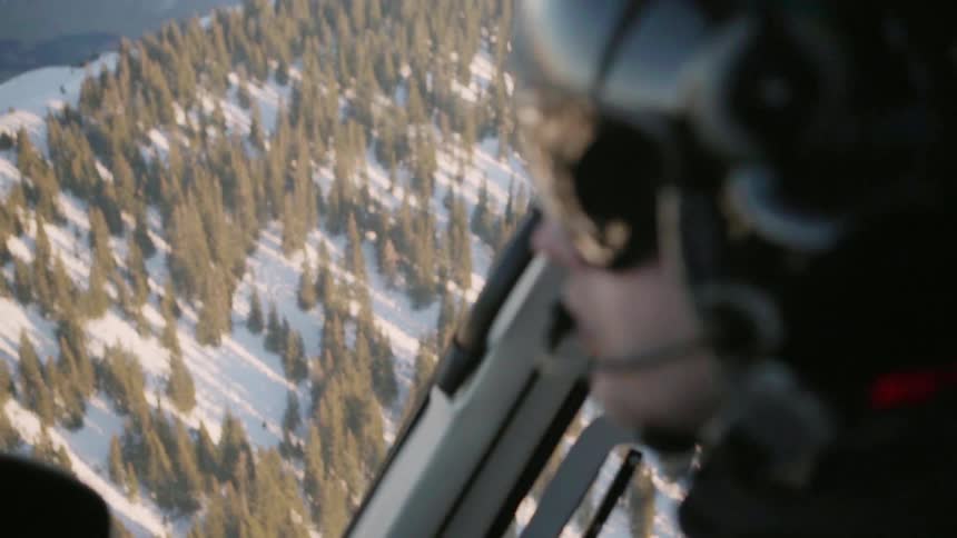 A helicopter is piloted over snowy mountains