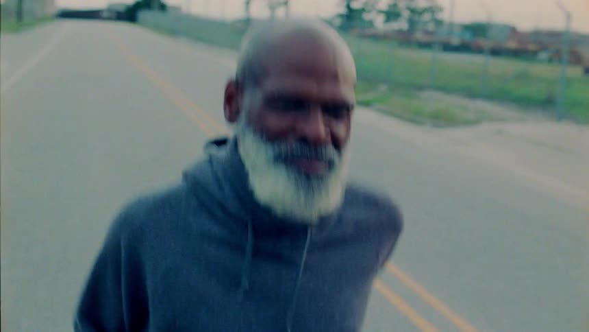 An older man is jogging down the middle of the road