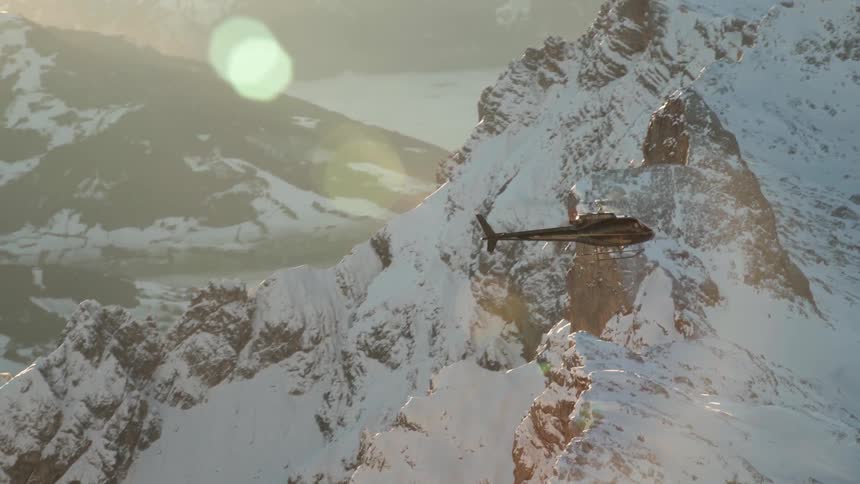 A helicopter flies over snowy mountains