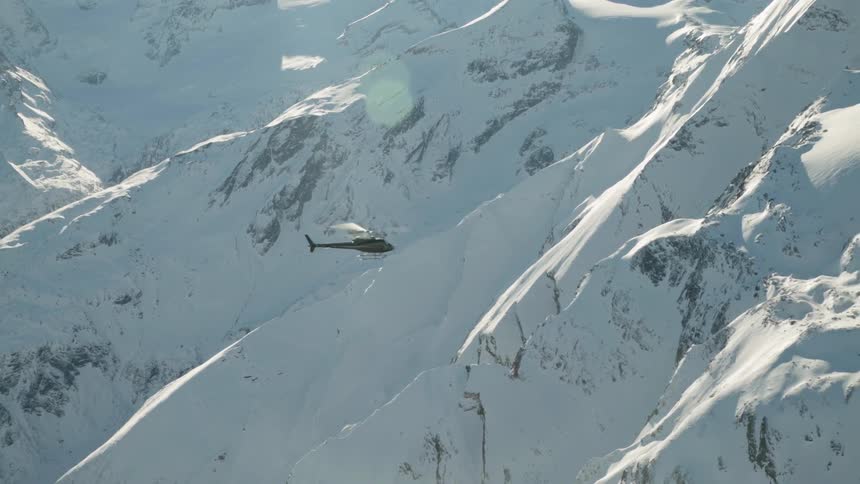 A helicopter flies over snowy mountains