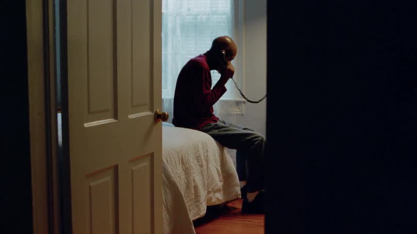 A man talks on a corded phone from a bed