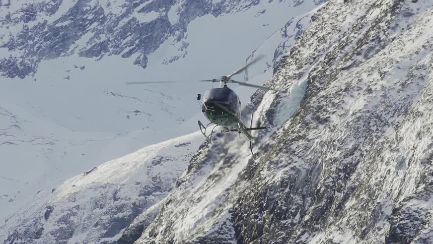 A helicopter is piloted over snowy mountains