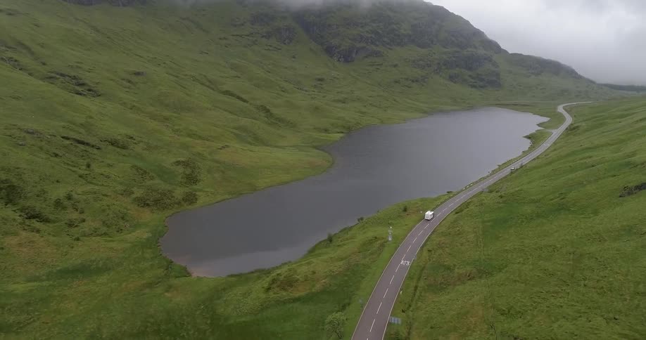 A truck hauling a trailer travels through a valley road