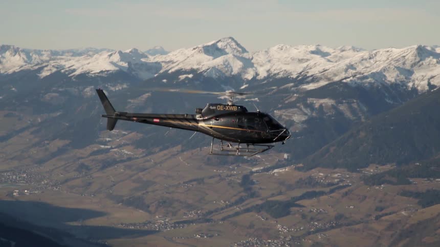 A black helicopter lowers down towards the mountains