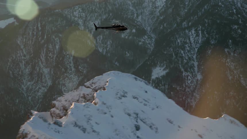 A helicopter flies up near the tall snowy mountains