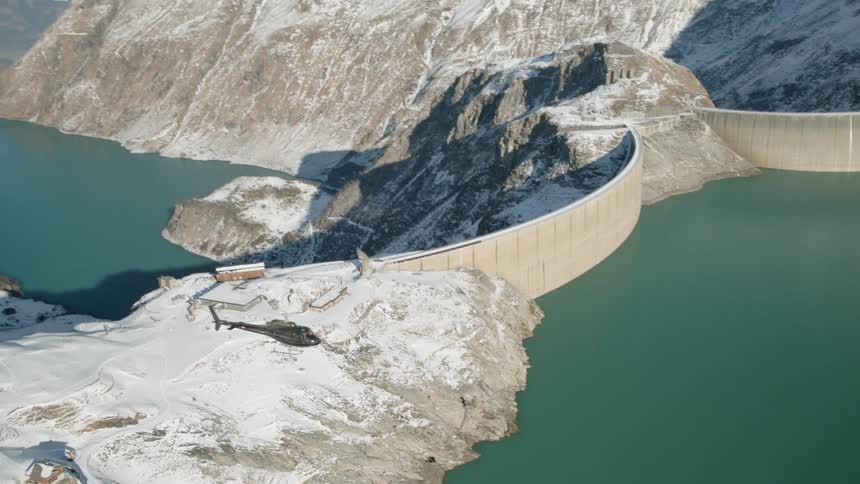 A helicopter flies over a dam in the winter