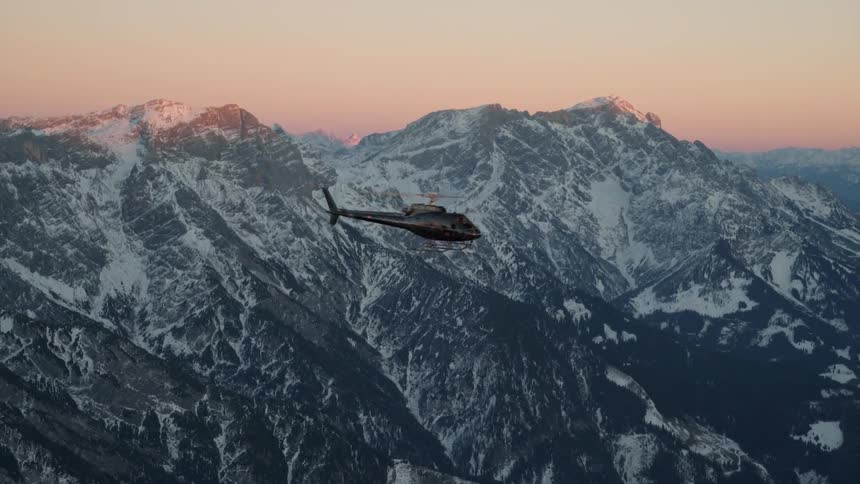 A helicopter is flying above some snow covered mountains