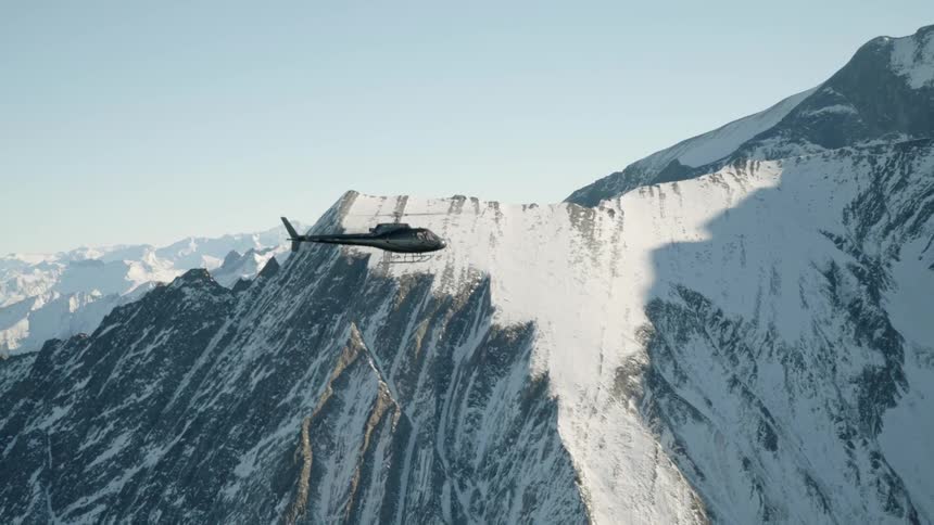 A helicopter flies above a snow covered mountain range during the day