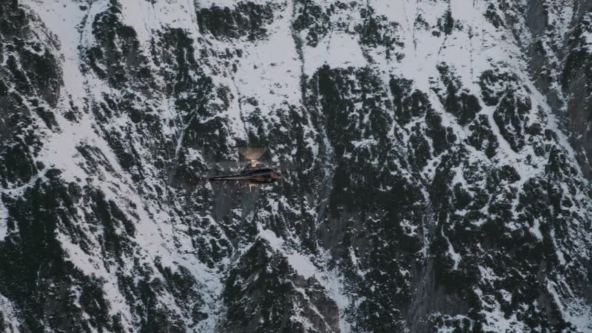 A helicopter flies above mountains