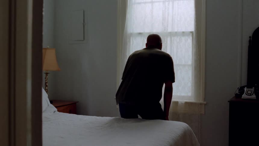 Man stands in a bedroom and sits on the bed