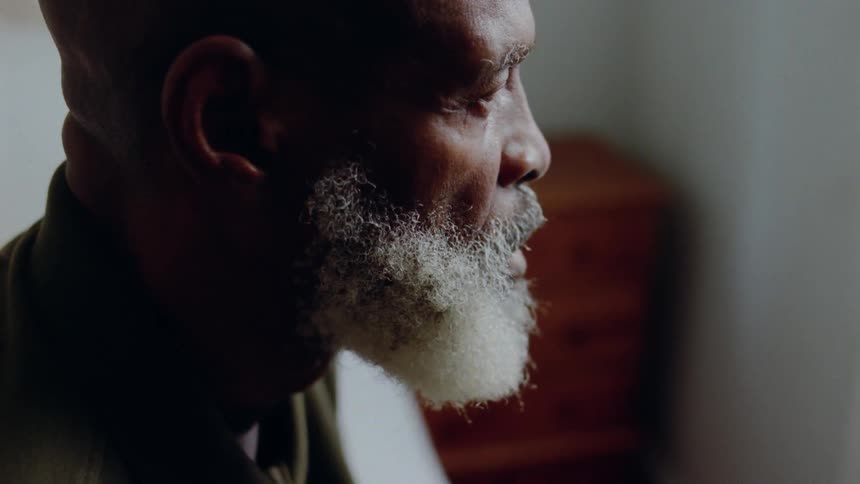 A bearded man looks solemnly in a bedroom