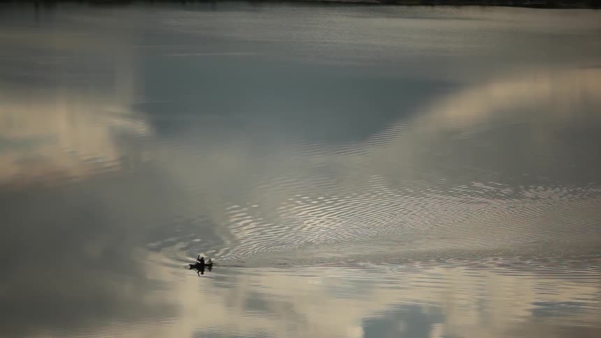 Someone rowing a boat in a body of water partially covered by low-lying clouds