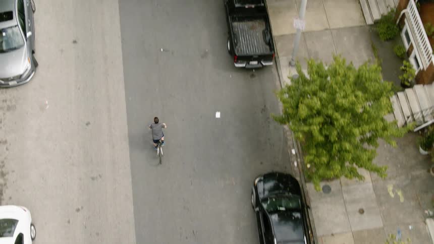 Man pedals bike down the middle of a road lined with cars