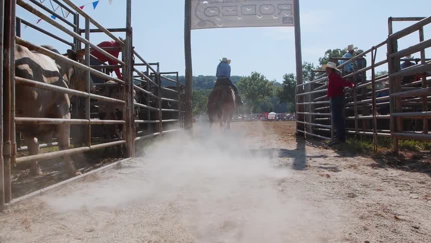 A cowgirl on a horse gallops out into a rodeo ring on a sunny day