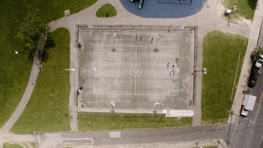 People play on an outdoor basketball court on a sunny day