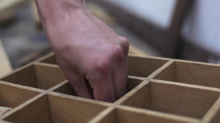Hand dips into a wooden crate and takes out wood shavings