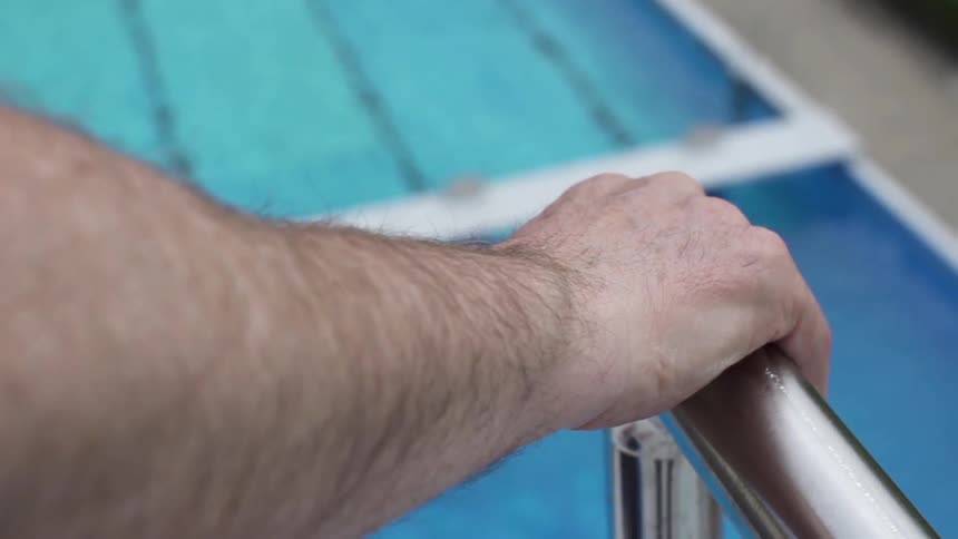 A swimmer grips the railing at a diving platform