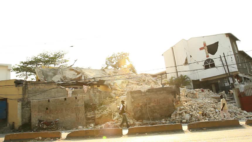People walking down a sidewalk in front of a dilapidated building