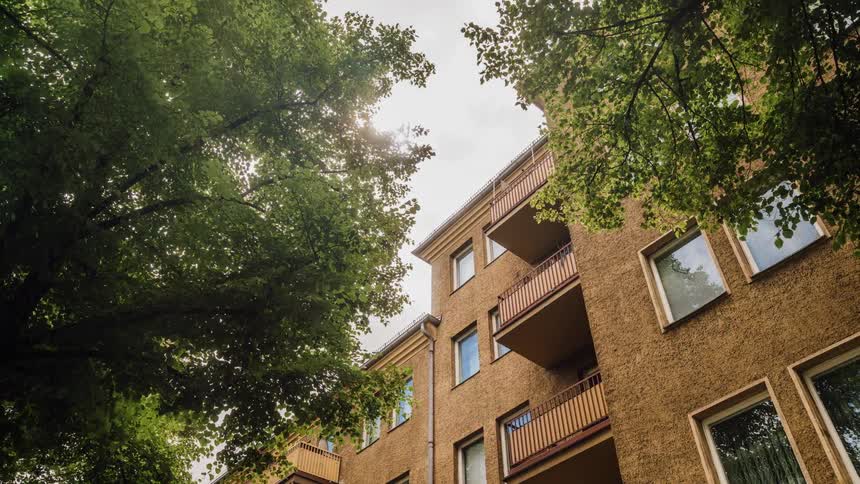 Clouds drift over an apartment complex and trees during the day