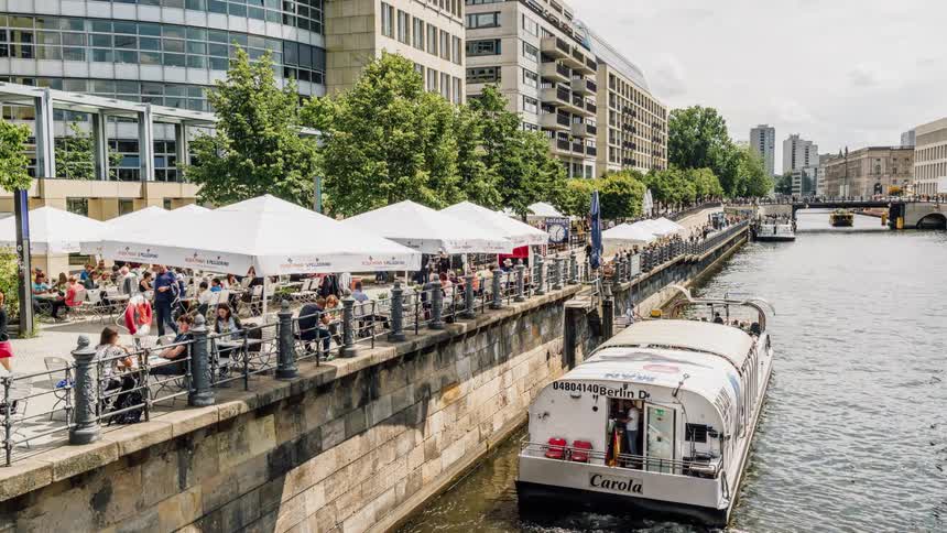 People sit travel and get in boats by a canal in a city