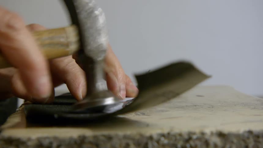 A cobbler is using a hammer on a piece of cut leather
