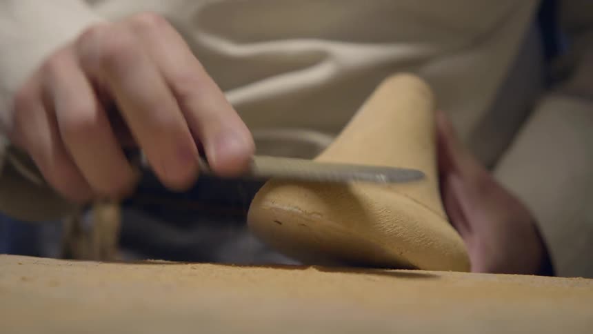 A cobbler is sanding a shoe form