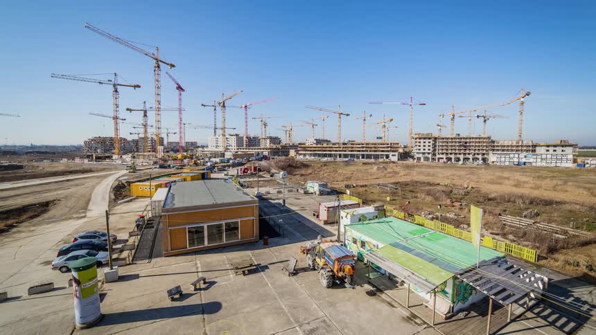 The work site has many cranes moving and cars driving