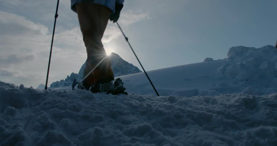A person hikes up a snowy hill with snow shoes on