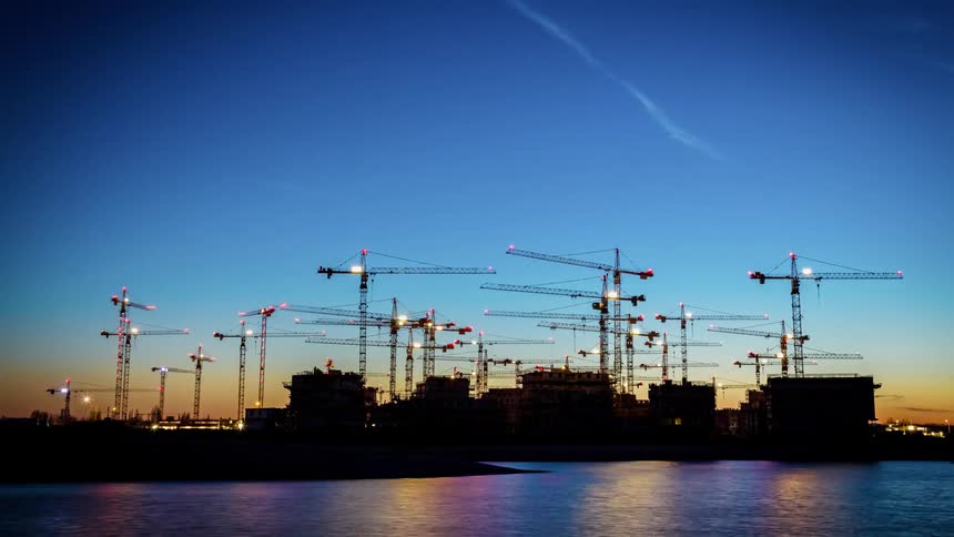 Cranes rotate and are lit up with colored lights at dusk