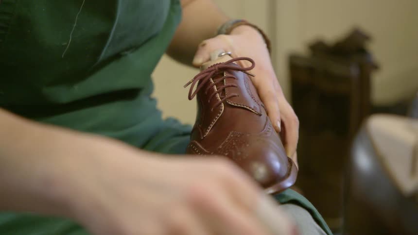 A cobbler is polishing a pair of shoes during the day