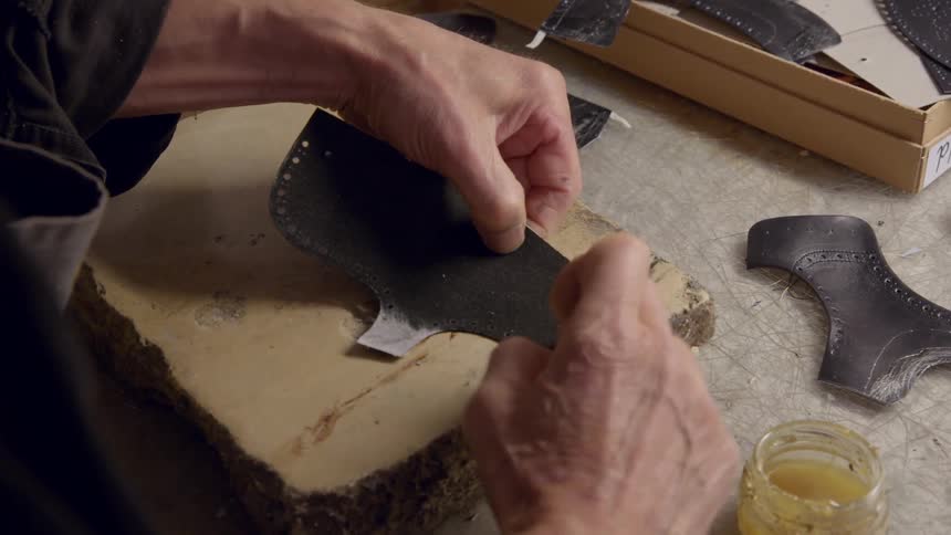 A cobbler applies adhesive to a piece of shoe