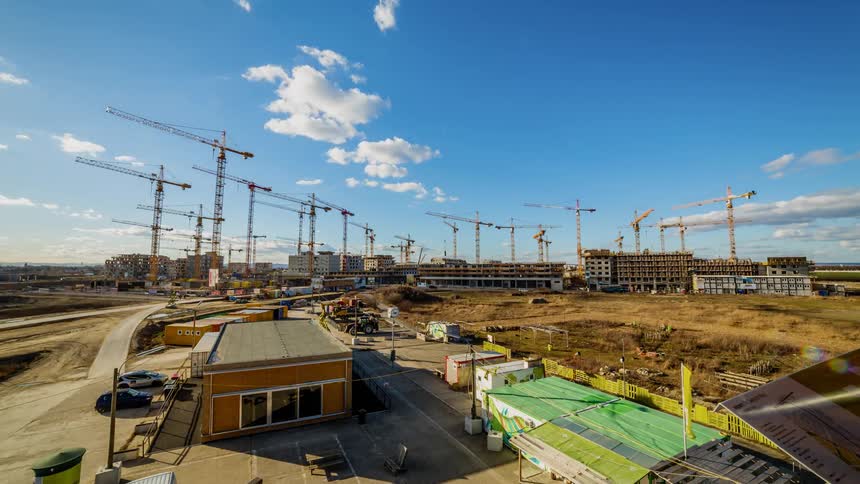 Workers and cranes move at a construction site as the day passes