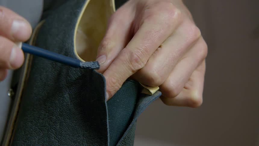 A cobbler is brushing a substance onto the edges of a shoe he is making