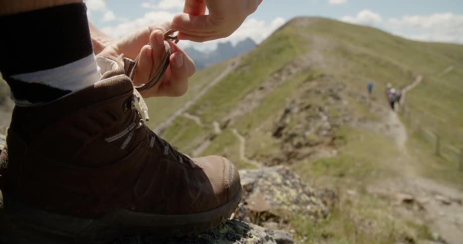 A hiker ties their boots atop a hill