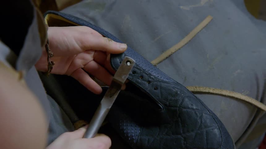 Person punches eyelet holes into a shoe they are making