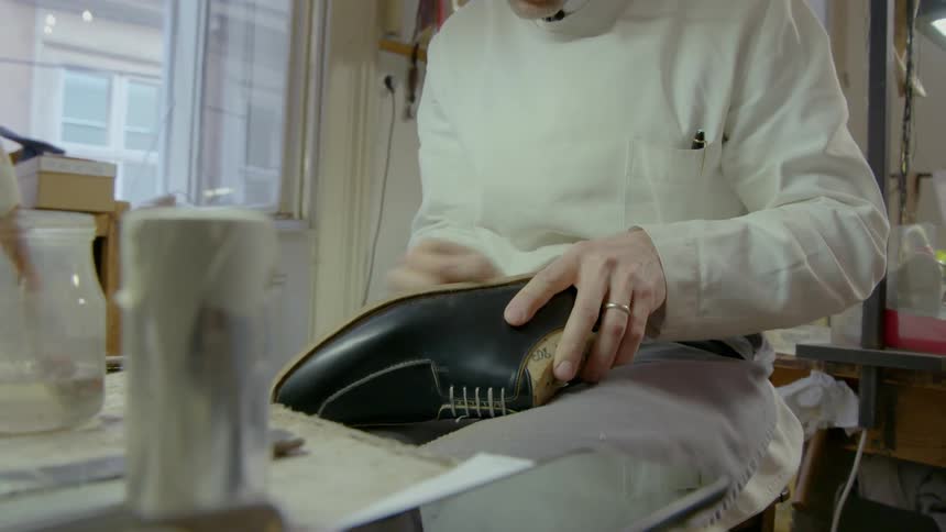 A cobbler is working on a shoe he is making during the day