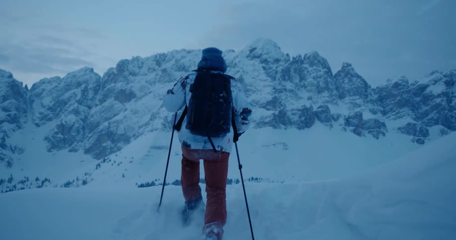 A man is walking in the snow towards a large mountain