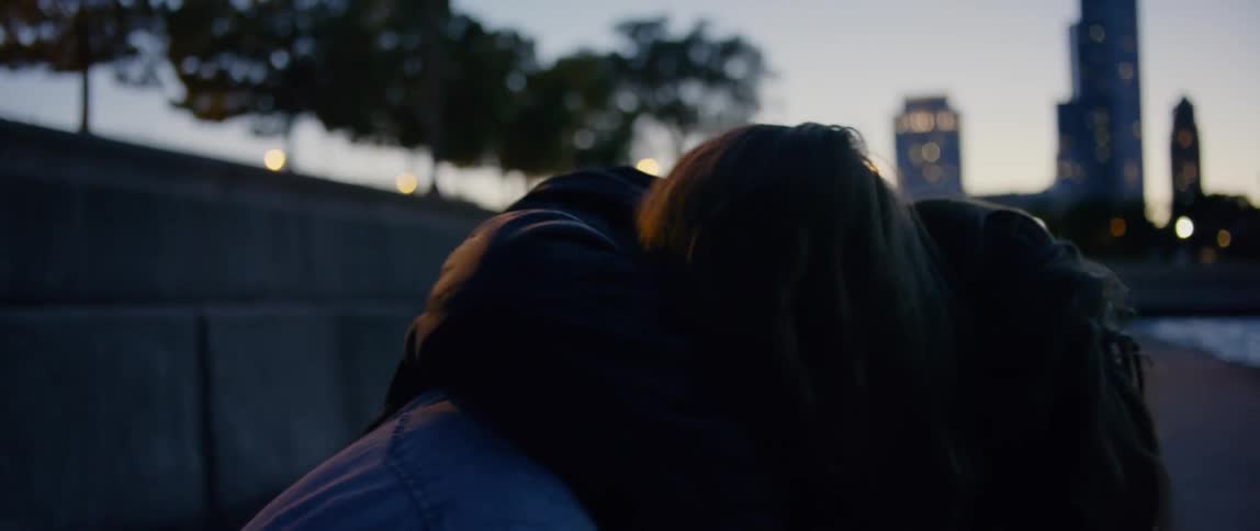 A young woman sitting on the sidewalk is joined by a man