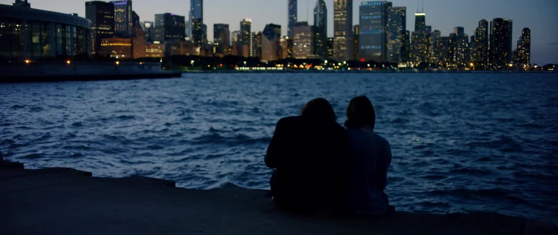 Someone is sitting on the edge of the river overlooking the city