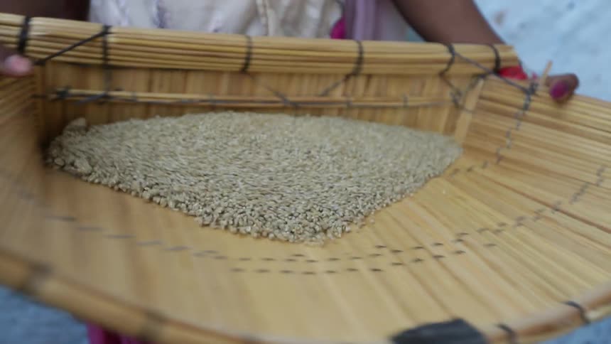 A woman sifting pebbles in a bamboo tray