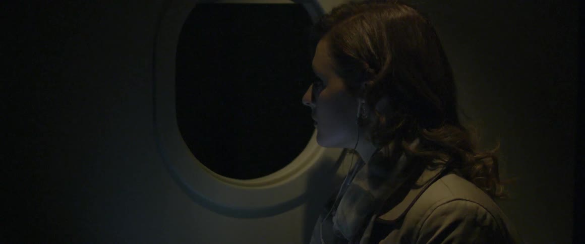 Woman looks out airplane window at night