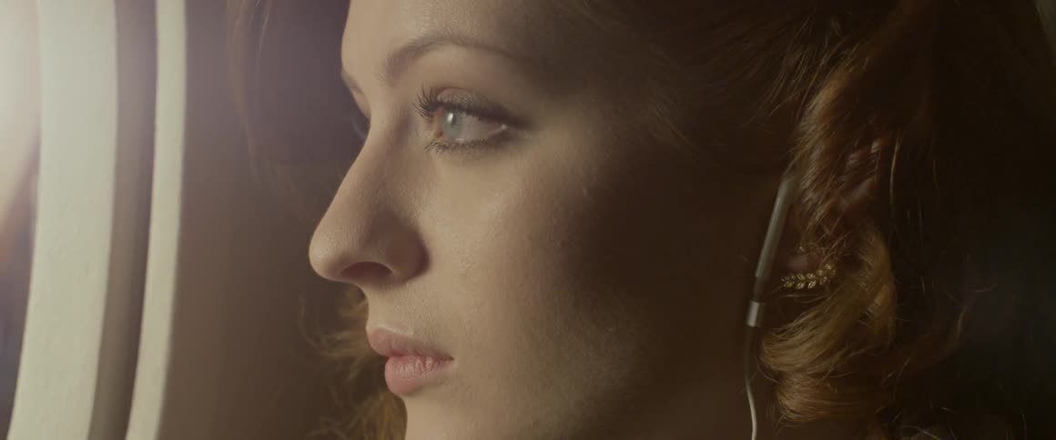 Woman looks out a window while wearing headphones