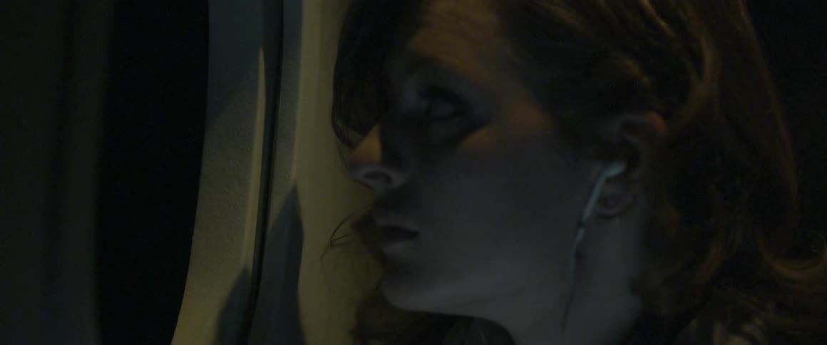 A woman is looking out of an airplane window at night