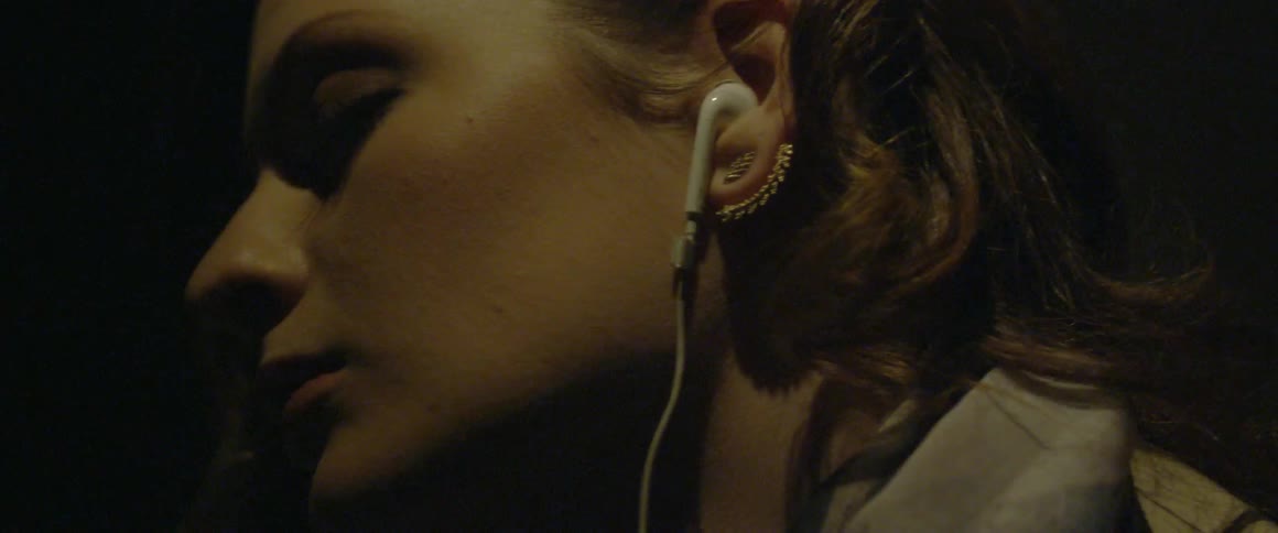 A woman wearing earbuds is sleeping on a plane at night