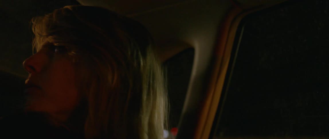 A woman rides in the back of a car at night