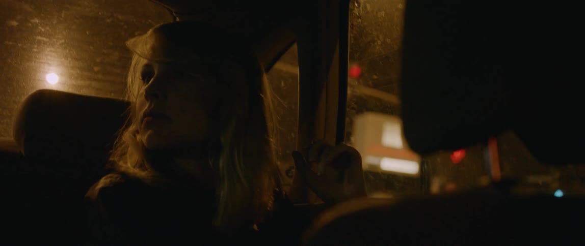 Woman rides in the back of a car through a city at night