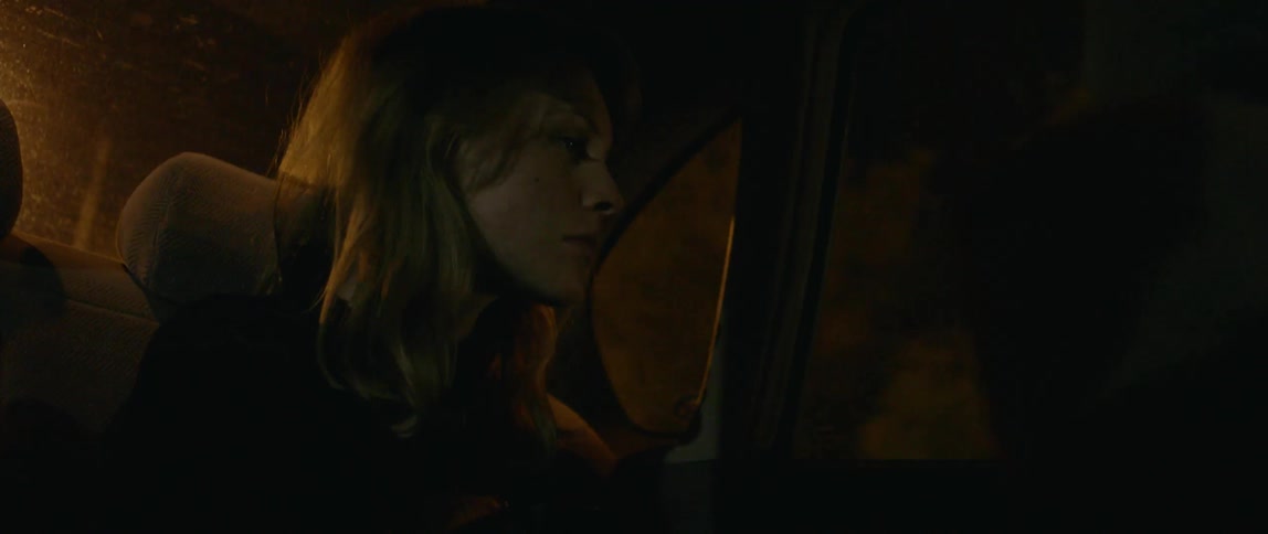 A woman rides in the back of a car at night