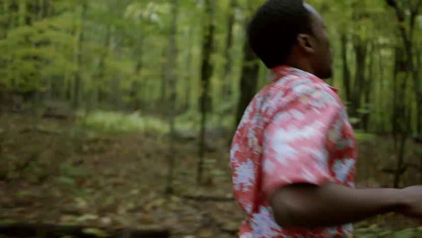 A young man jogs through a forest during the day