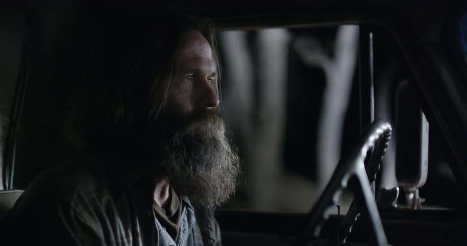 A bearded man sits in the front seat of a car