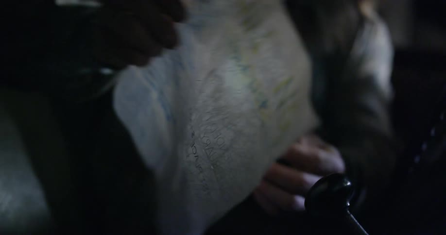 Someone is sitting and picks up a piece of paper with a map drawn on it